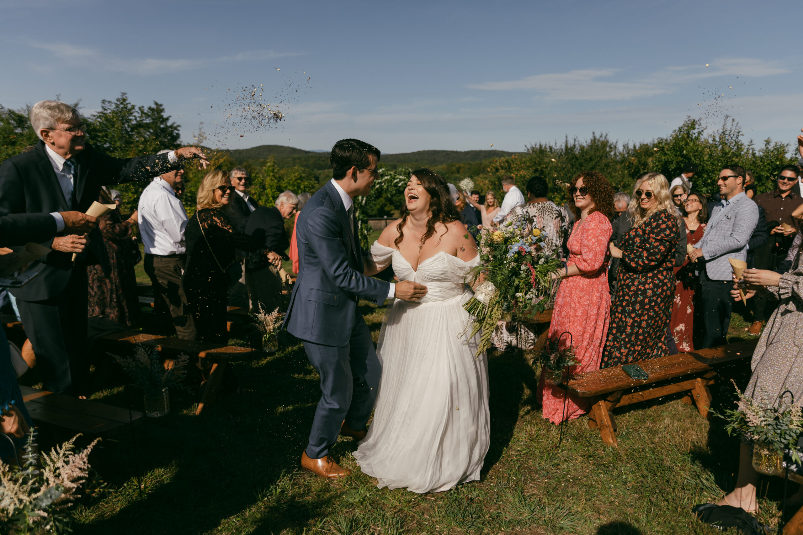 bride and groom laugh while guests throw dried flowers at them post ceremony